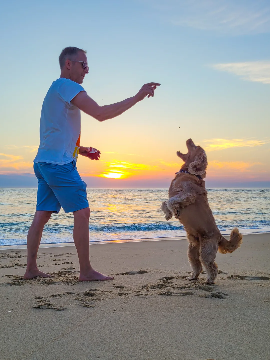 Jens Depenau spielt bei Sonnenuntergang am Strand mit seinem Hund Bruno, der freudig hochspringt